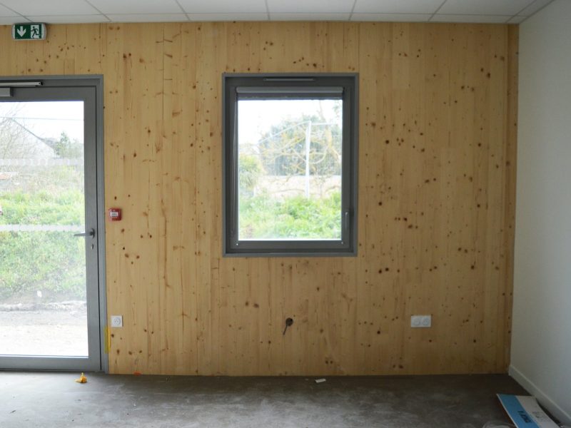 Mur intérieur en panneaux de bois naturel avec porte-fenêtre et fenêtre à cadre gris dans un espace en construction
