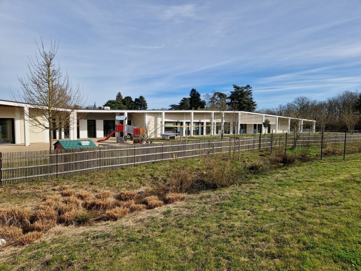 École maternelle moderne avec préau à claire-voie, façades claires et aire de jeux, entourée d'un jardin et d'arbres