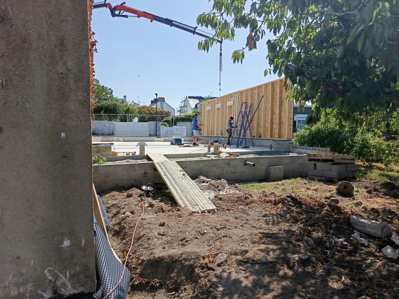 Construction d'une maison ossature bois avec fondations béton, grue de chantier et échafaudage visible