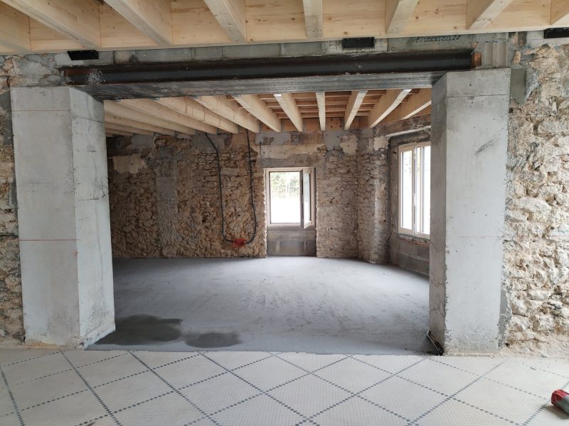 Rénovation intérieure avec structure bois neuve, murs en pierre apparente et béton, sol en cours d'aménagement