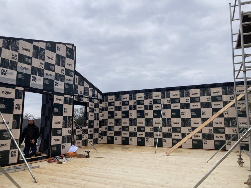 Construction d'ossature bois avec panneaux isolants NUCK en damier noir et beige, chantier en cours sous ciel nuageux