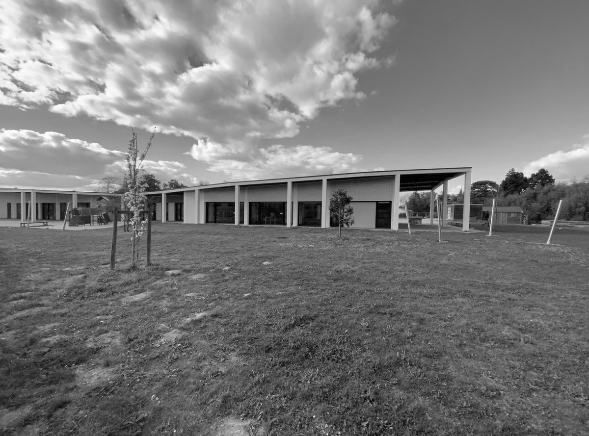 Bâtiment moderne en béton avec colonnade et grandes ouvertures, façade linéaire donnant sur un terrain herbeux avec jeunes arbres