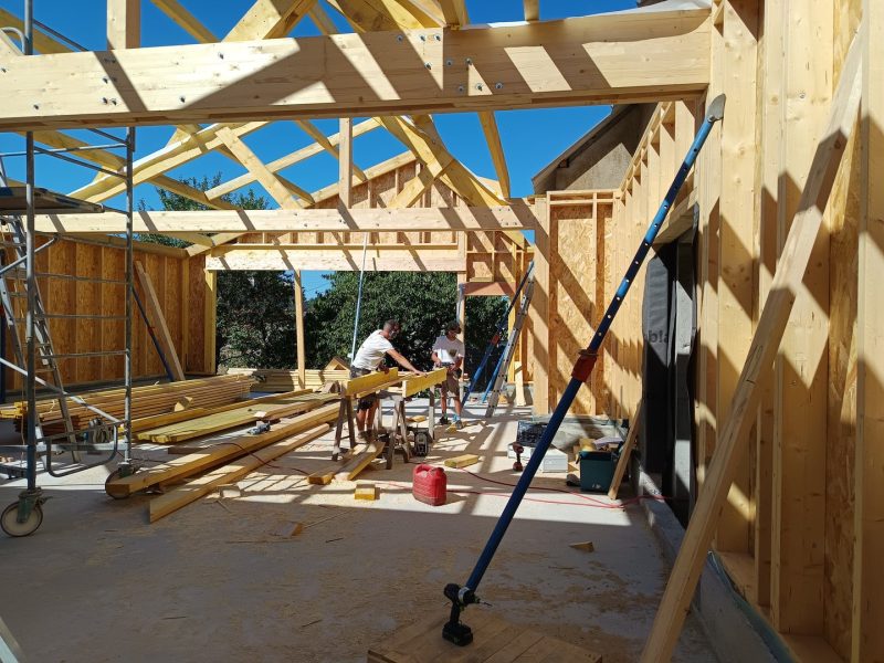 Chantier de construction en ossature bois avec poutres apparentes et panneaux OSB sous ciel bleu