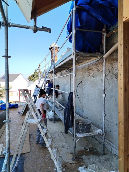 Rénovation de façade en béton avec échafaudage, ouvriers appliquant enduit extérieur sur mur fissuré