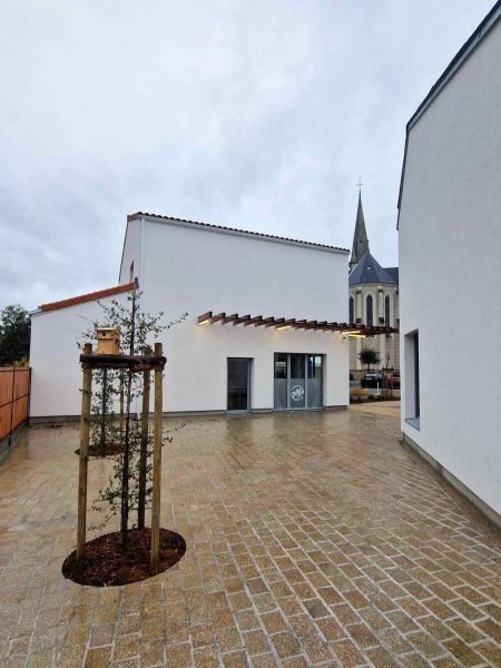 vue de côté du bâtiment avec l'église en fond et une place public en premier plan