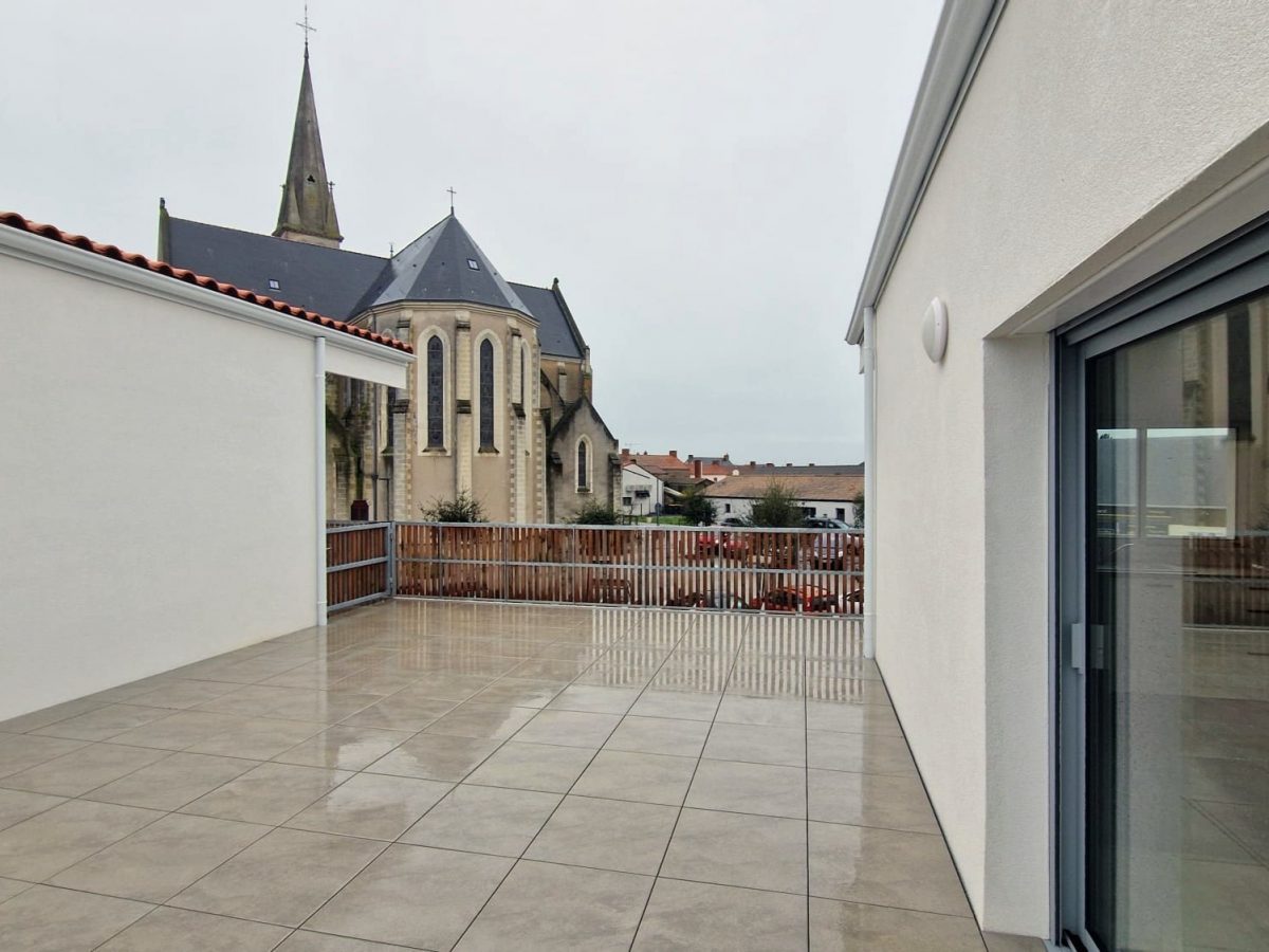 vue de l'église depuis la terrasse des logements en dalle de carrelage, garde-corps en bois, bâtiments enduit blanc