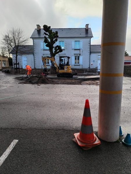 Maison en pierre rénovée avec volets bleus, chantier de terrassement en cours, grue et ouvrier en gilet orange