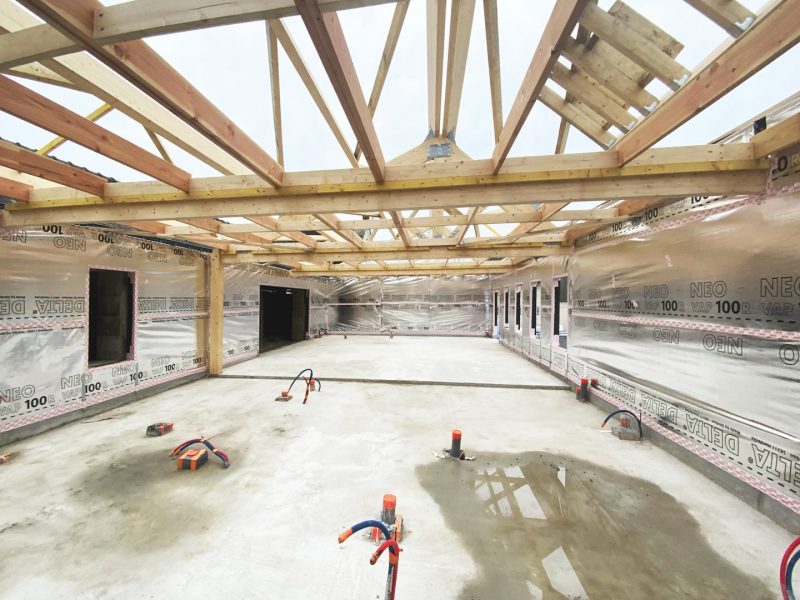 Charpente bois apparente en construction avec membranes pare-vapeur sur les murs, sol béton brut et outils de chantier
