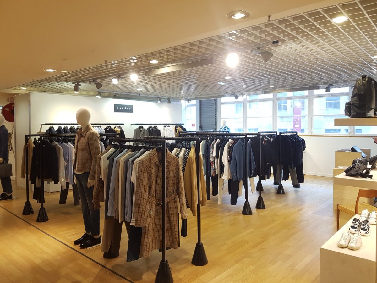 Intérieur de boutique de vêtements avec plafond à grille métallique, parquet bois, rails noirs et vitrines modernes