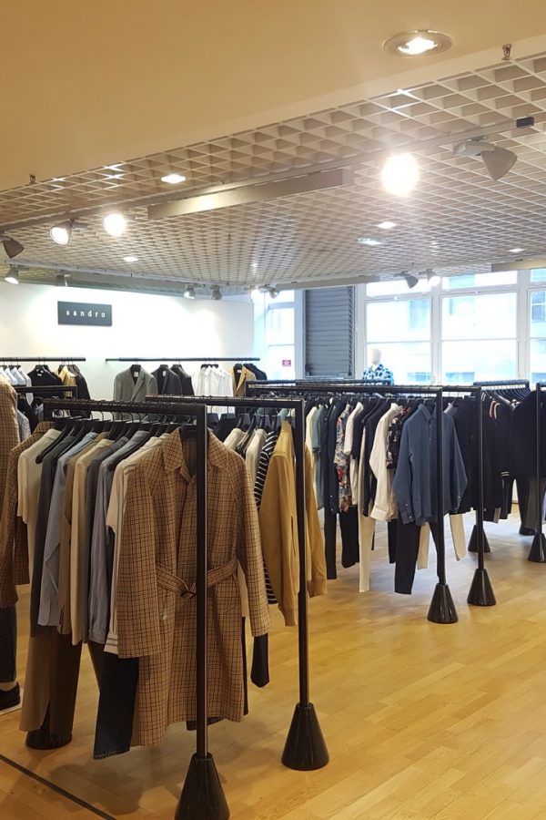 Intérieur de boutique de vêtements avec plafond à grille métallique, parquet bois, rails noirs et vitrines modernes