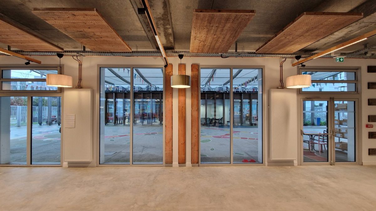Espace intérieur industriel avec poutres bois apparentes, plafond béton brut, grandes baies vitrées et luminaires suspendus