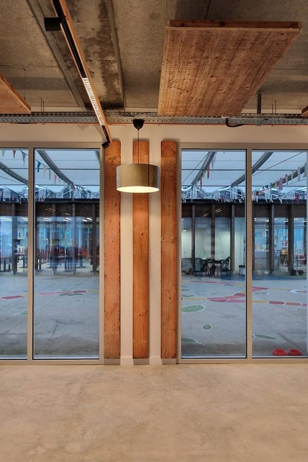 Espace intérieur industriel avec poutres bois apparentes, plafond béton brut, grandes baies vitrées et luminaires suspendus