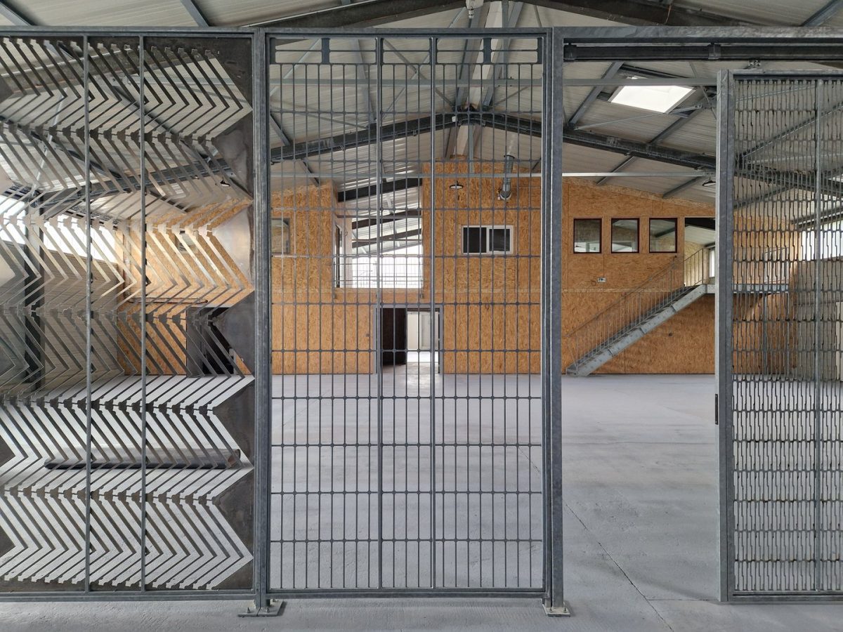Porte coulissante en acier avec grille verticale ouvrant sur un espace industriel avec murs en OSB et structure métallique