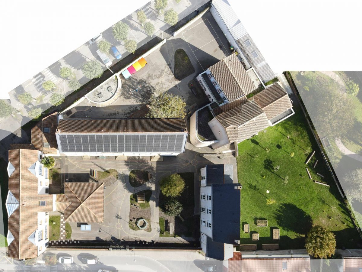 Vue aérienne d'un ensemble architectural avec bâtiments à toits en tuiles, espaces verts, cours intérieures et panneaux solaires