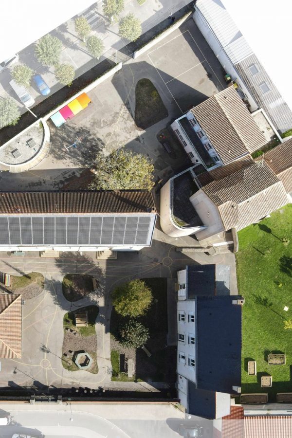 Vue aérienne d'un ensemble architectural avec bâtiments à toits en tuiles, espaces verts, cours intérieures et panneaux solaires