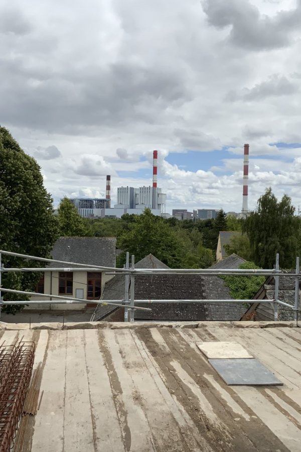 Chantier de rénovation d'une toiture avec échafaudages, vue sur usine industrielle avec cheminées en arrière-plan