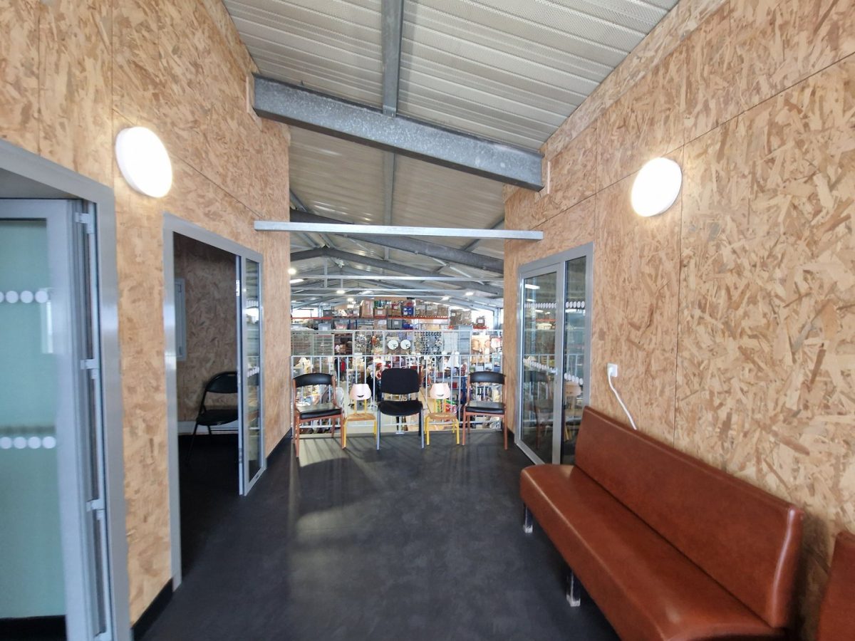 Espace intérieur avec murs en contreplaqué OSB, portes vitrées, plafond métallique et vue sur un entrepôt industriel