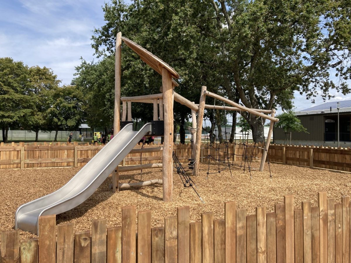 Aire de jeux en bois naturel avec toboggan et structures d'escalade, délimitée par une palissade en bois