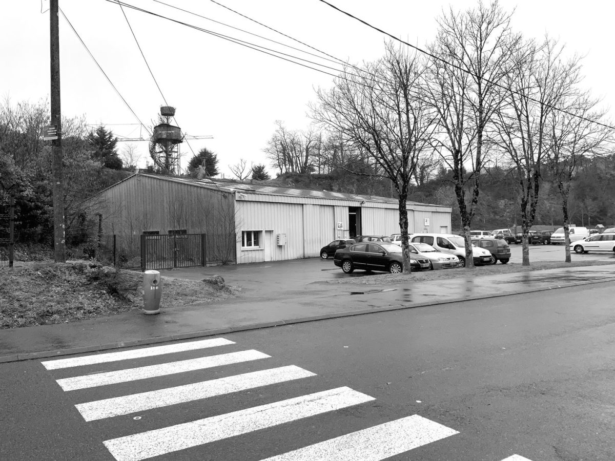 Bâtiment préfabriqué à bardage métallique avec parking et arbres dénudés, traversé par des lignes électriques aériennes