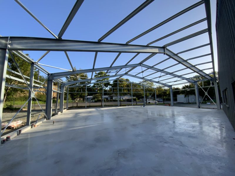 Charpente métallique apparente d'un bâtiment en construction avec dalle béton, structure en acier gris sous ciel bleu