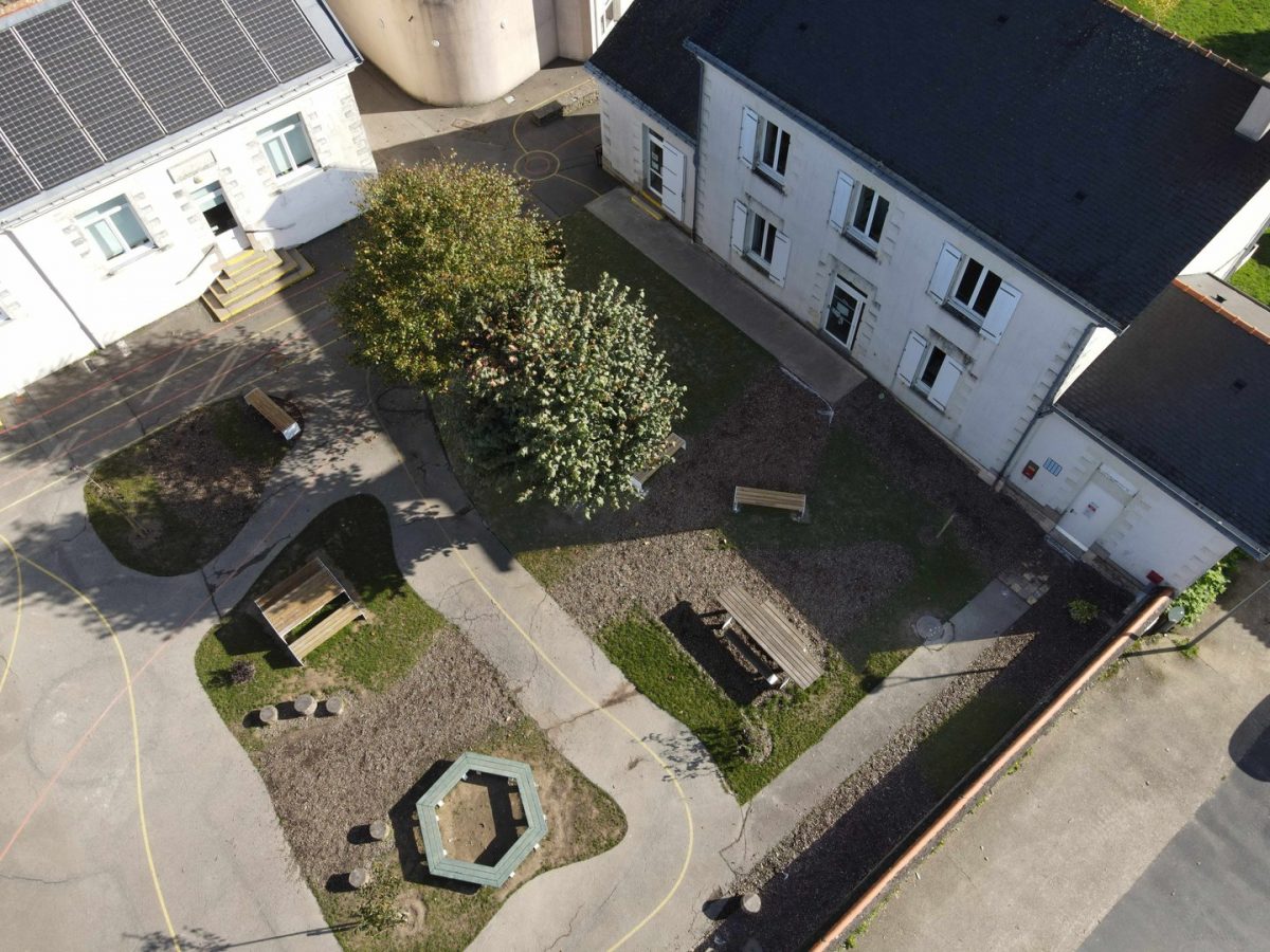 Vue aérienne d'une cour intérieure avec bâtiments blancs, toitures sombres, espaces verts et panneaux solaires