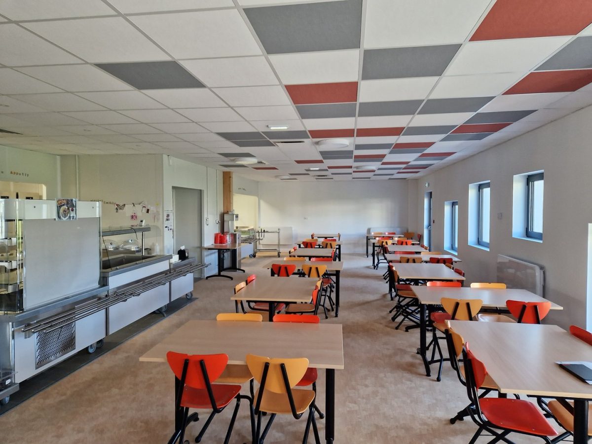 Réfectoire moderne avec plafond acoustique coloré rouge et gris, tables en bois et chaises orange, espace de restauration scolaire
