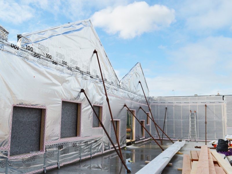 Construction d'une maison unifamiliale avec ossature bois, enveloppée de membrane protectrice, fenêtres en cours d'installation