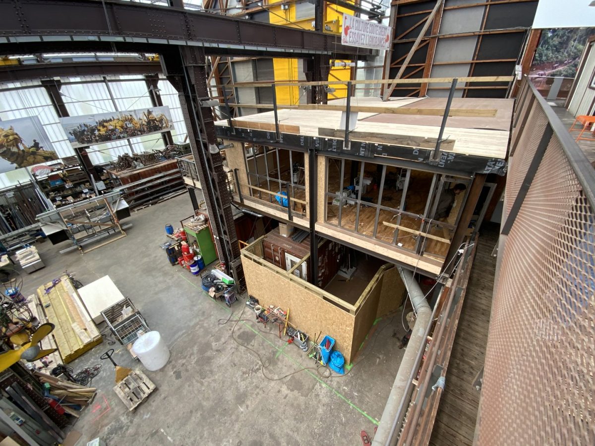 Structure multi-niveaux en bois en construction dans un atelier industriel avec poutres métalliques et baies vitrées
