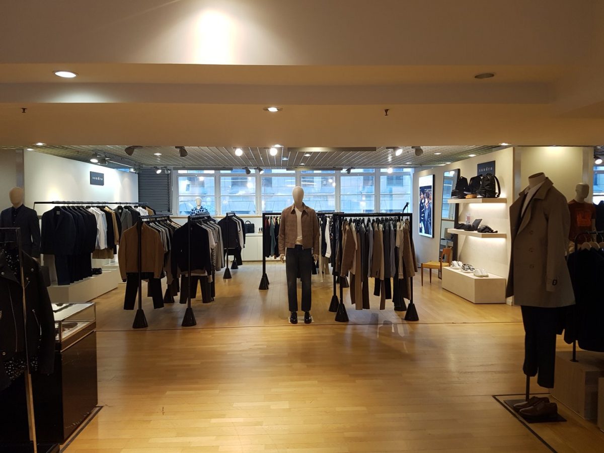 Intérieur de boutique contemporaine avec parquet bois, plafond suspendu métallique, éclairage encastré et présentoirs de vêtements