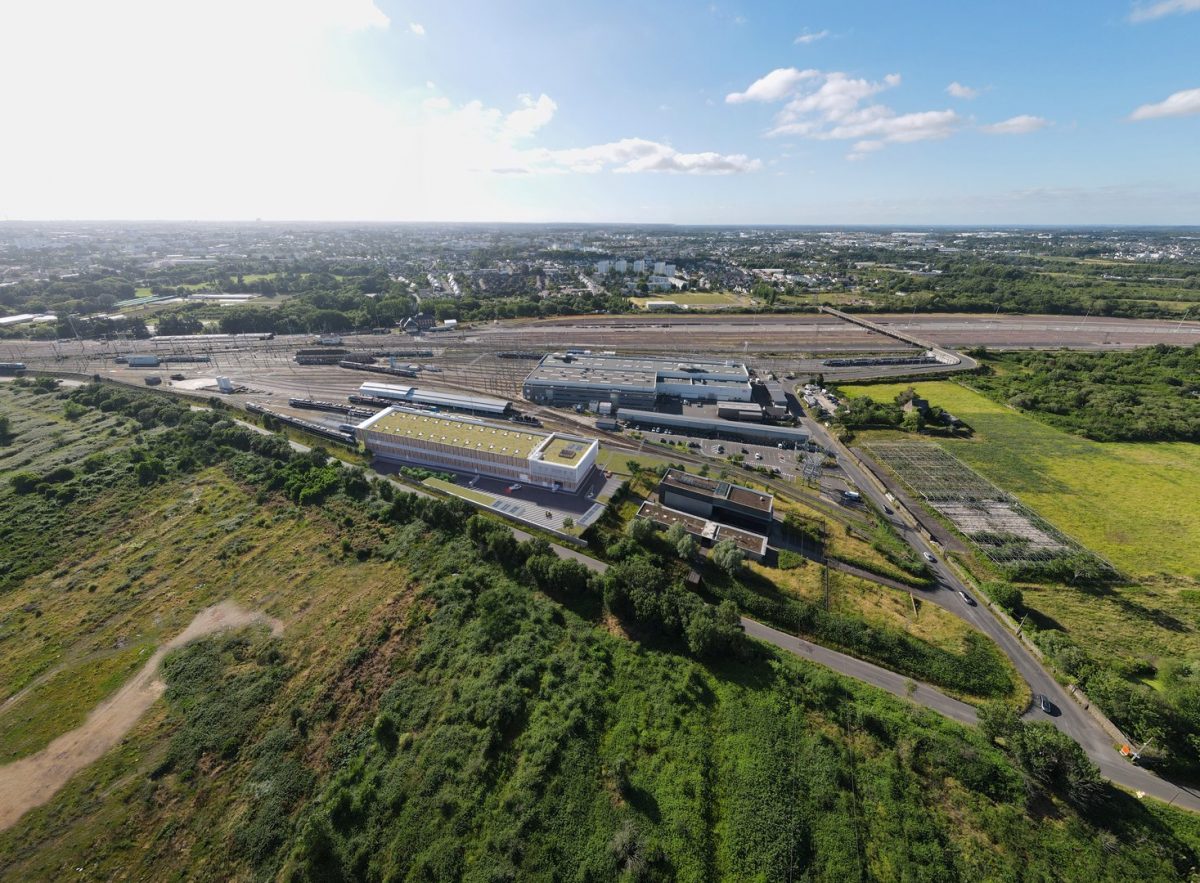 Vue aérienne d'un complexe industriel moderne avec toiture végétalisée, entouré de voies ferrées et d'espaces verts