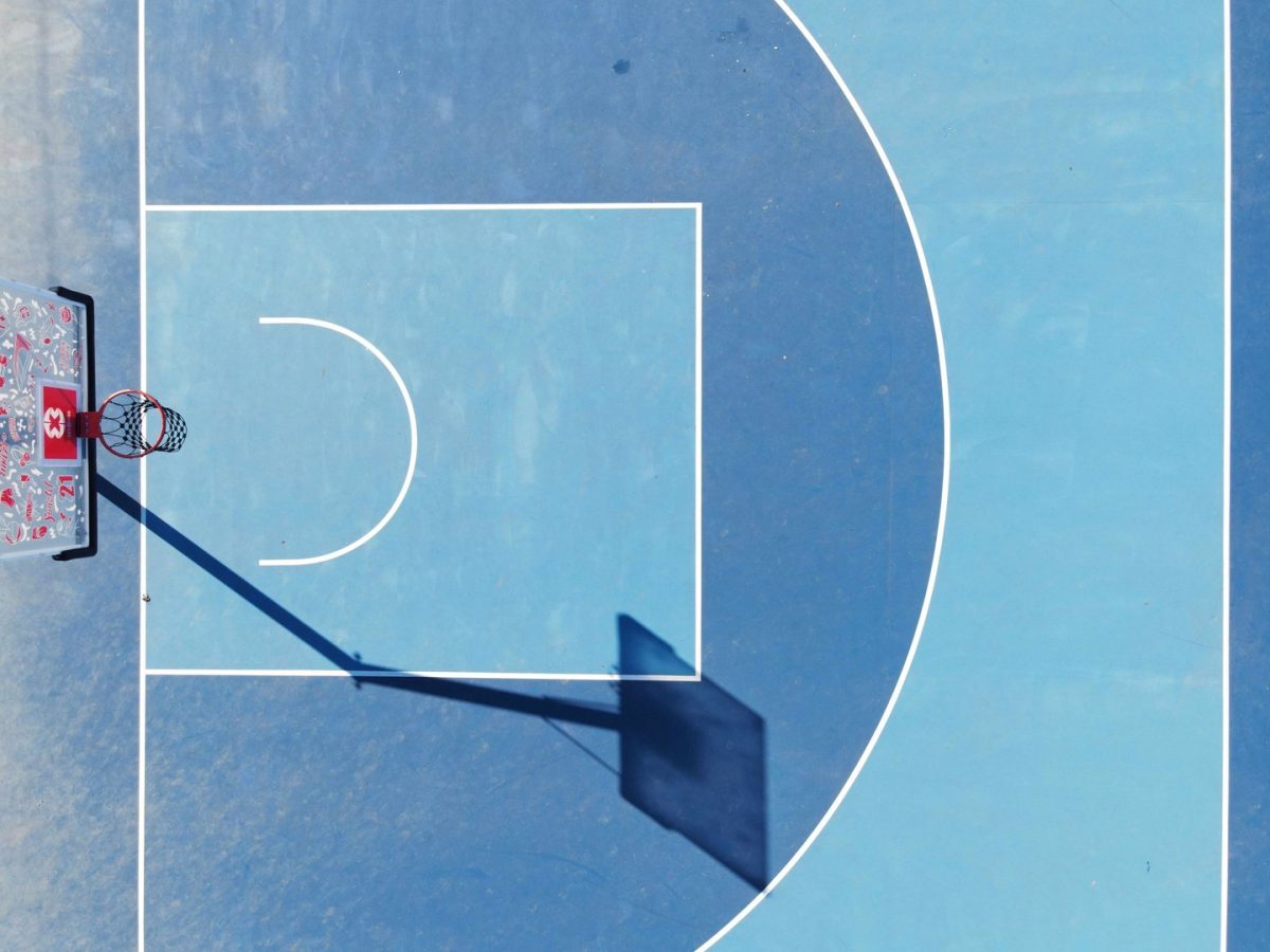 Vue aérienne d'un terrain de basketball bleu avec marquages blancs, panier et son ombre portée