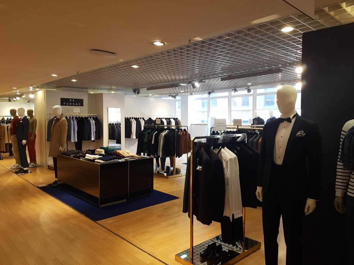 Intérieur de boutique de vêtements masculins avec plafond à grille métallique, plancher bois, mannequins et présentoirs