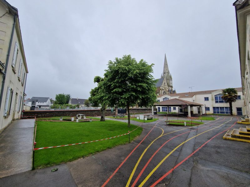 Place publique avec église à flèche, espaces verts, arbres et bâtiments résidentiels sous ciel nuageux