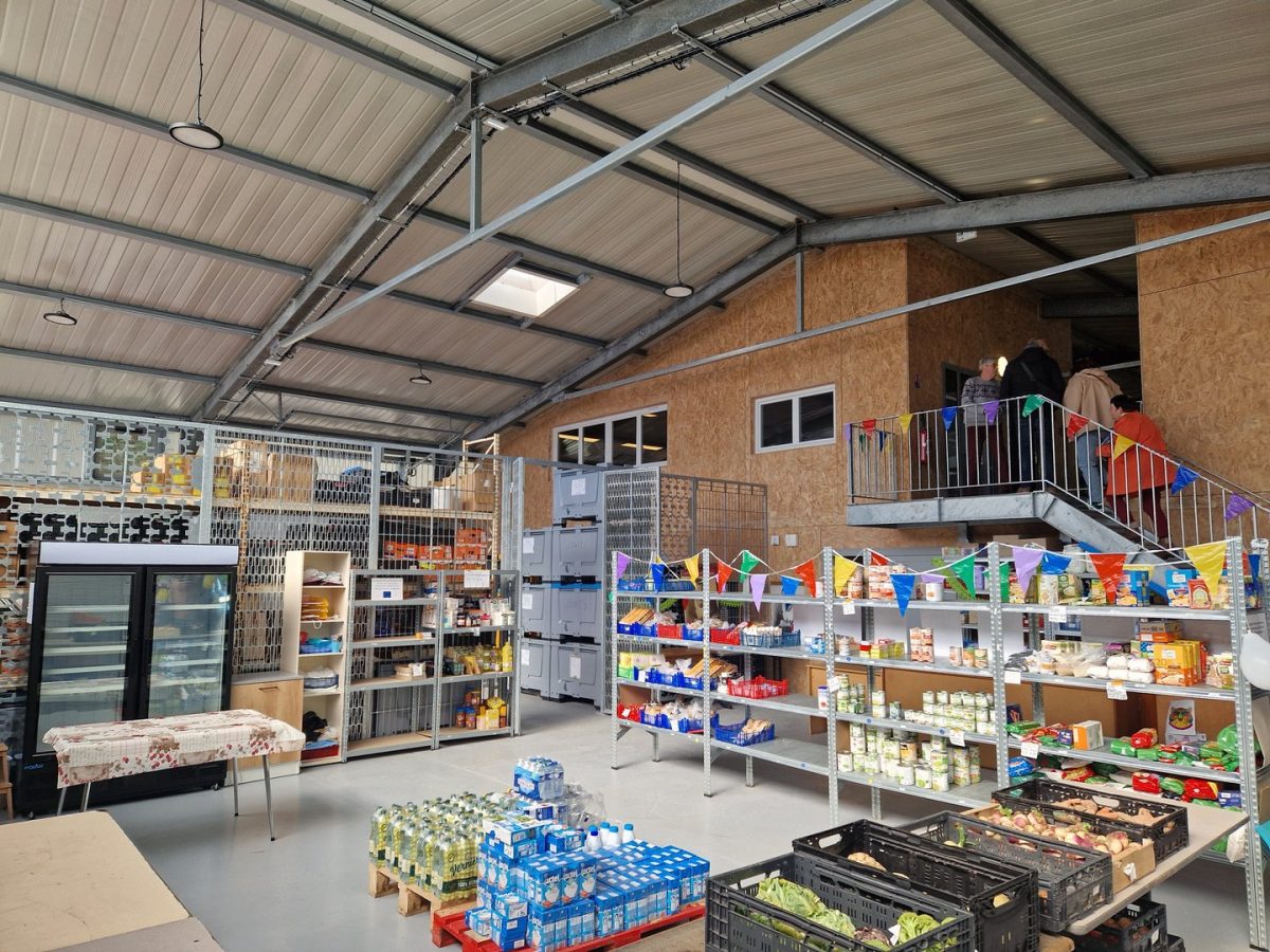 Intérieur d'un espace communautaire avec charpente métallique apparente, mezzanine en bois et étagères de stockage alimentaire