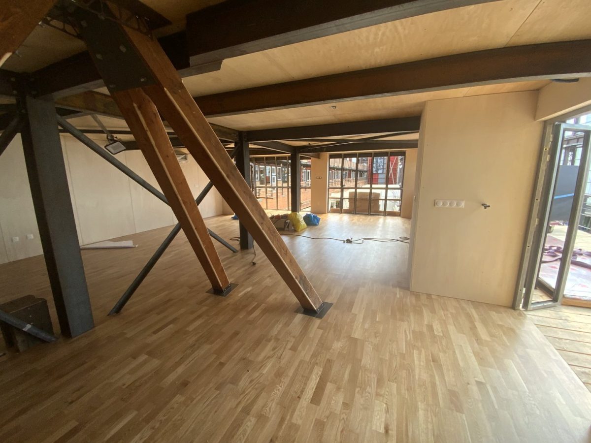 Espace sous combles avec poutres bois apparentes, charpente mixte bois-métal, parquet clair et grande baie vitrée