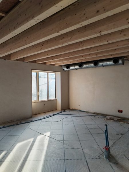 Plafond avec poutres en bois apparentes et plancher chauffant en cours d'installation dans un espace en rénovation
