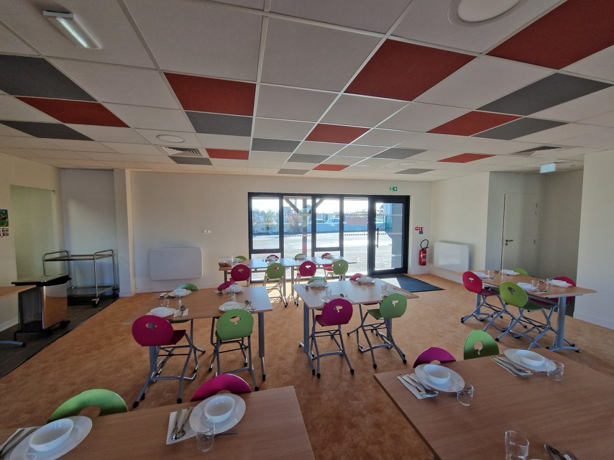 Salle de restauration avec plafond acoustique coloré rouge et gris, tables en bois et chaises multicolores