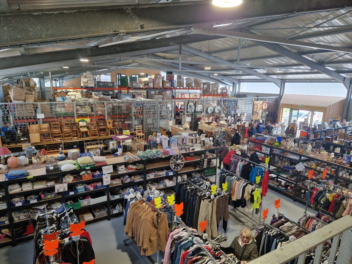 Intérieur d'un grand entrepôt commercial avec structure métallique apparente, étagères de marchandises diverses et vêtements