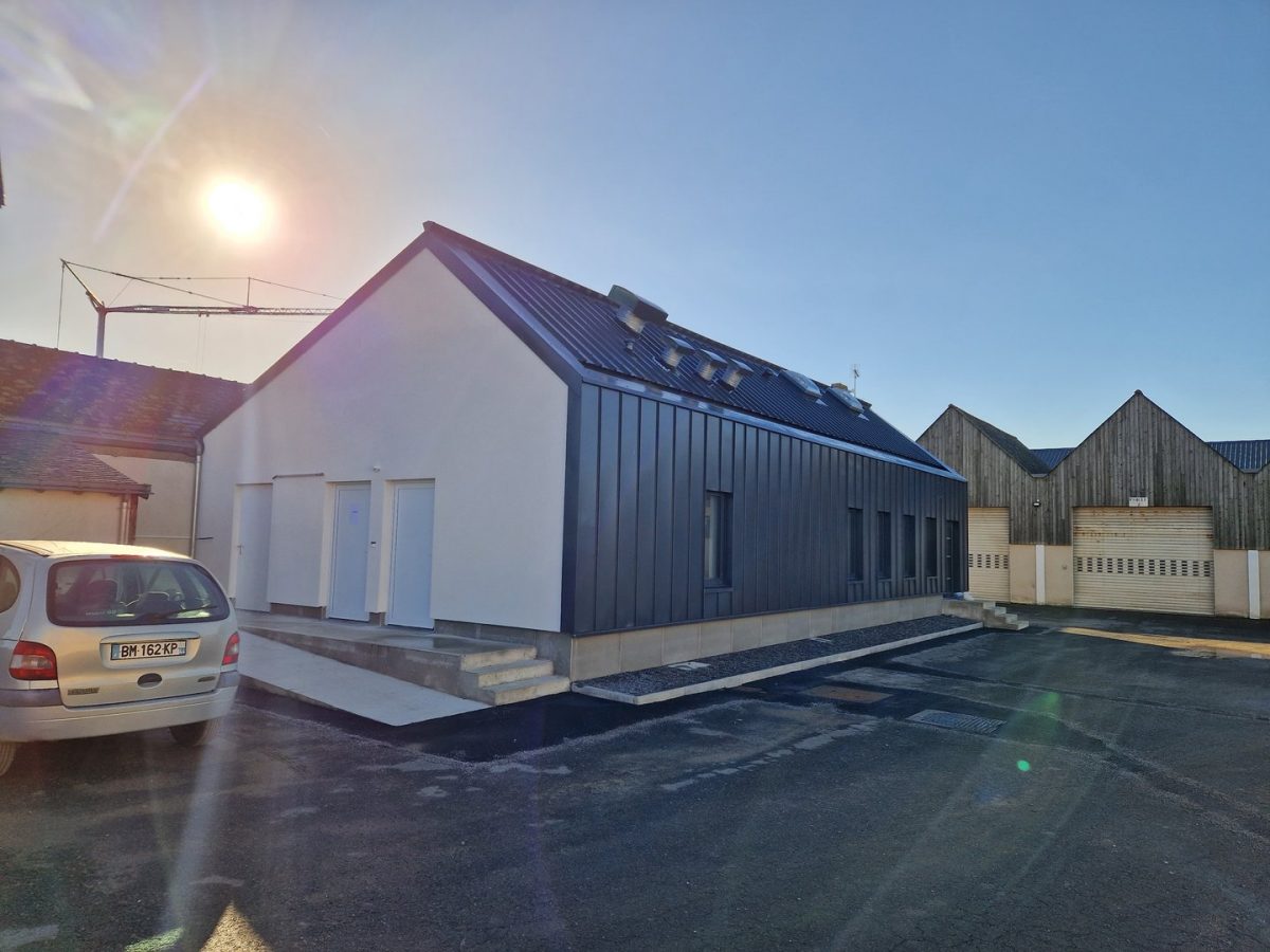 Bâtiment moderne à bardage métallique noir et façade blanche, toit en pente, situé dans un ensemble de constructions résidentielles