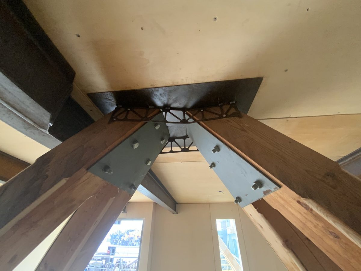 Détail de charpente en bois avec nœud structural métallique noir reliant plusieurs poutres apparentes au plafond