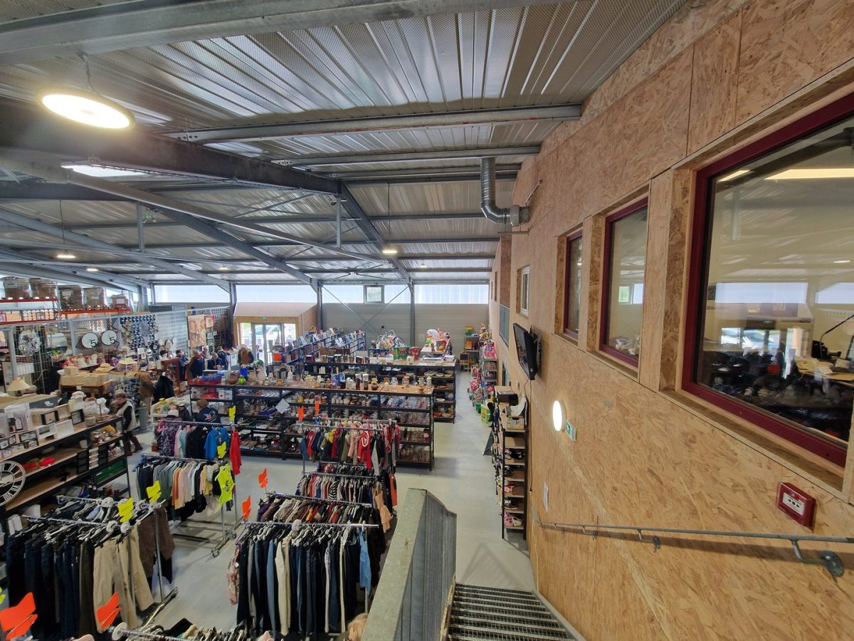 Intérieur d'un magasin avec structure métallique apparente, murs en OSB, mezzanine vitrée et rayonnages de vêtements