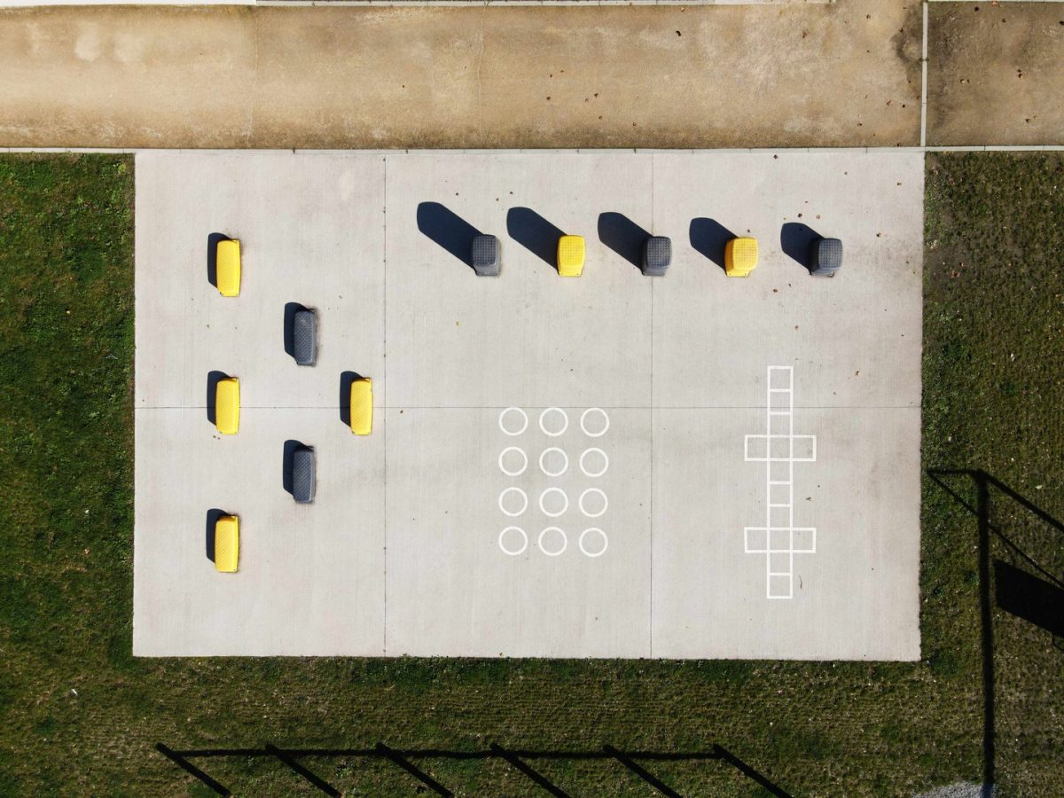 Vue aérienne d'une aire de jeux en béton avec assises jaunes et grises, motifs géométriques au sol