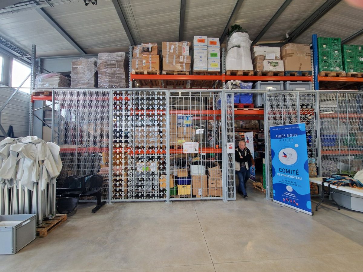 Entrepôt industriel avec mezzanine de stockage, cage grillagée et matériaux de construction organisés sur palettes