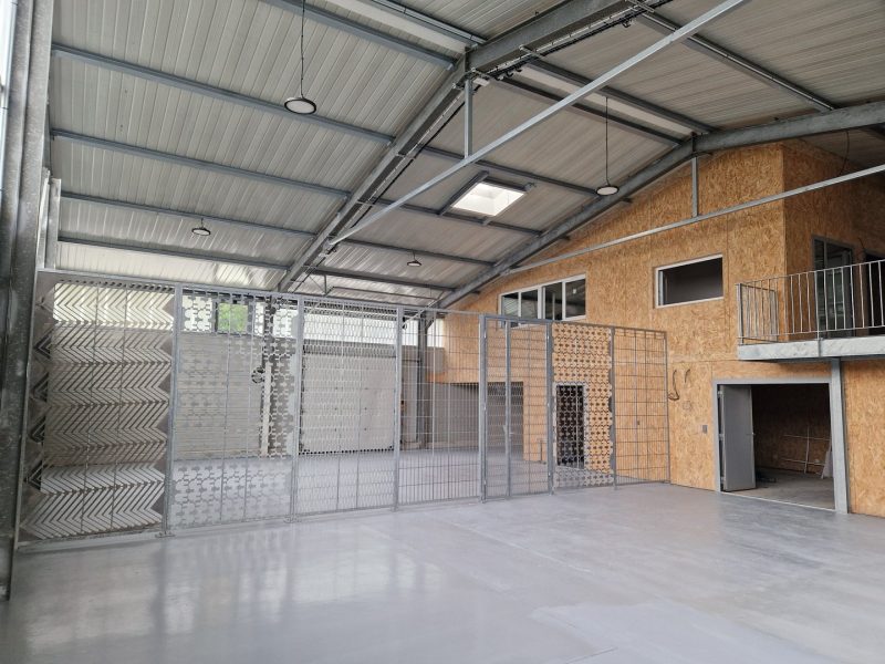 Hangar industriel avec structure métallique, plafond en tôle ondulée, mezzanine en bois OSB et panneaux d'exposition