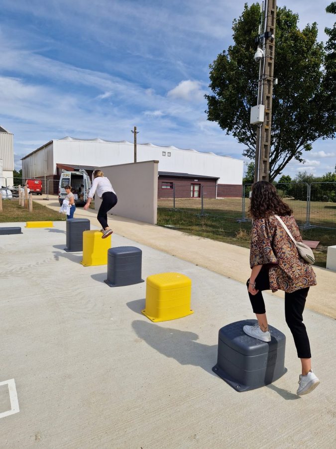 Blocs de jeu urbains jaunes et gris sur dalle béton, bâtiment blanc en arrière-plan, enfants jouant