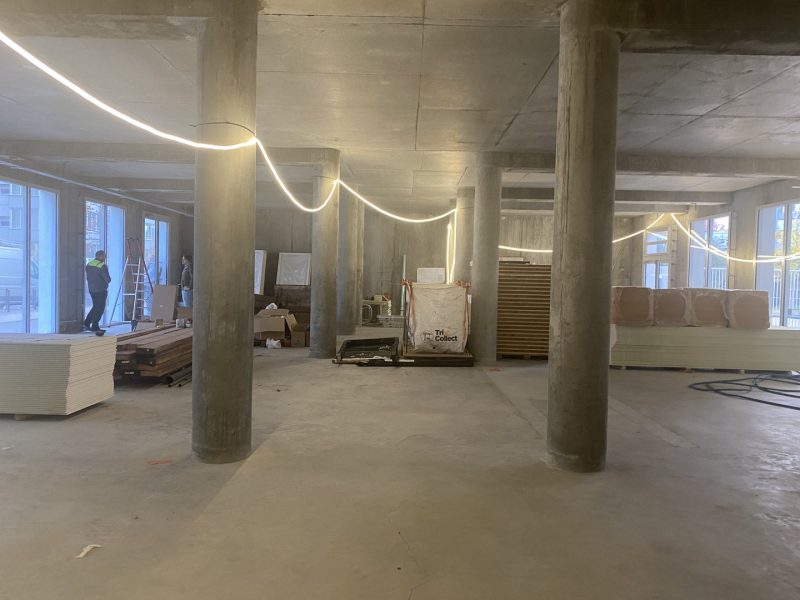 Espace intérieur en construction avec colonnes en béton brut, plafond structurel apparent et éclairage LED décoratif