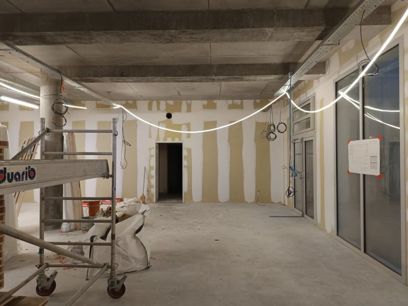Espace intérieur en construction avec plafond béton apparent, murs en plâtre, éclairage LED suspendu et échafaudage