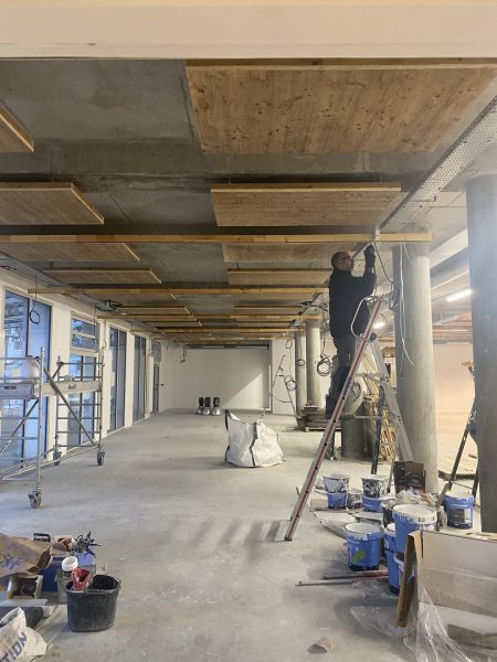 Rénovation de plafond en béton avec panneaux acoustiques en bois et ouvrier sur échelle