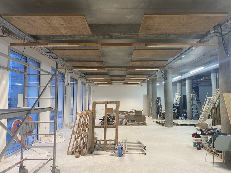 Espace commercial en construction avec plafond brut en béton, poutres en bois apparentes et baies vitrées industrielles