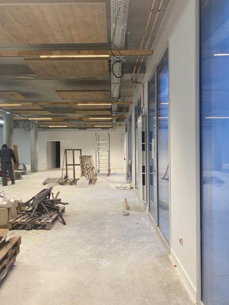 Espace commercial en rénovation avec plafond apparent, poutres en bois, éclairage LED et cloisons vitrées